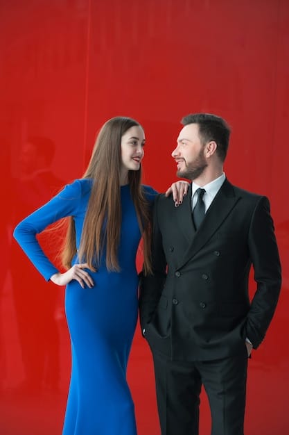 An image showing two actors smiling and holding hands on a red carpet. They are dressed in formal attire. The background is blurred, highlighting their expressions and posture.