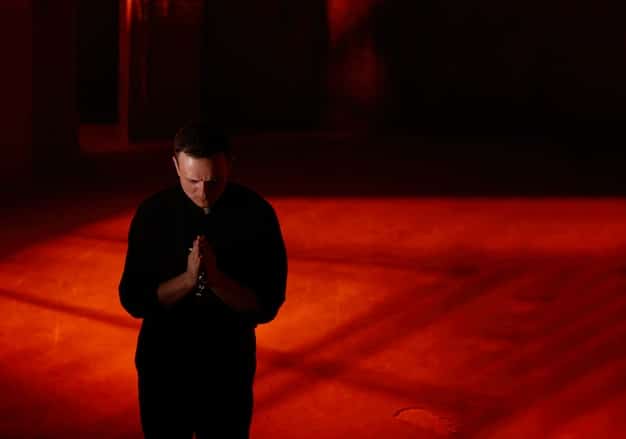 A dimly lit scene from a serious drama series, focusing on the intense facial expression of the lead actor.