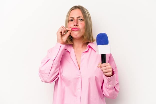 A close-up photo of a presenter looking uncomfortable holding an envelope, with another presenter whispering to them while holding a microphone.