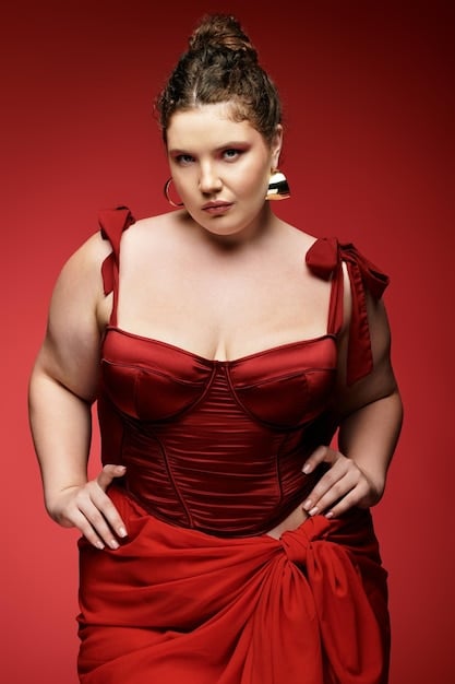 A plus-size model is confidently walking down a red carpet while wearing a custom-made gown made specifically for her body. The flash photography highlights the gown design and her natural glow.