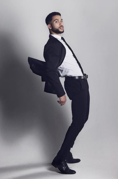 A full-length shot of a male celebrity wearing a suit with a unique, deconstructed design. The suit features visible stitching, raw edges, and an asymmetrical cut. He is accessorized with modern jewelry and minimalist shoes.