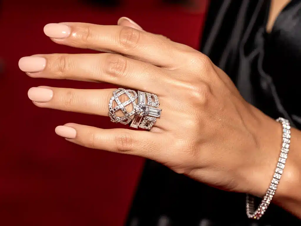 Celebrity hand showcasing intricate diamond ring and bracelet on red carpet.